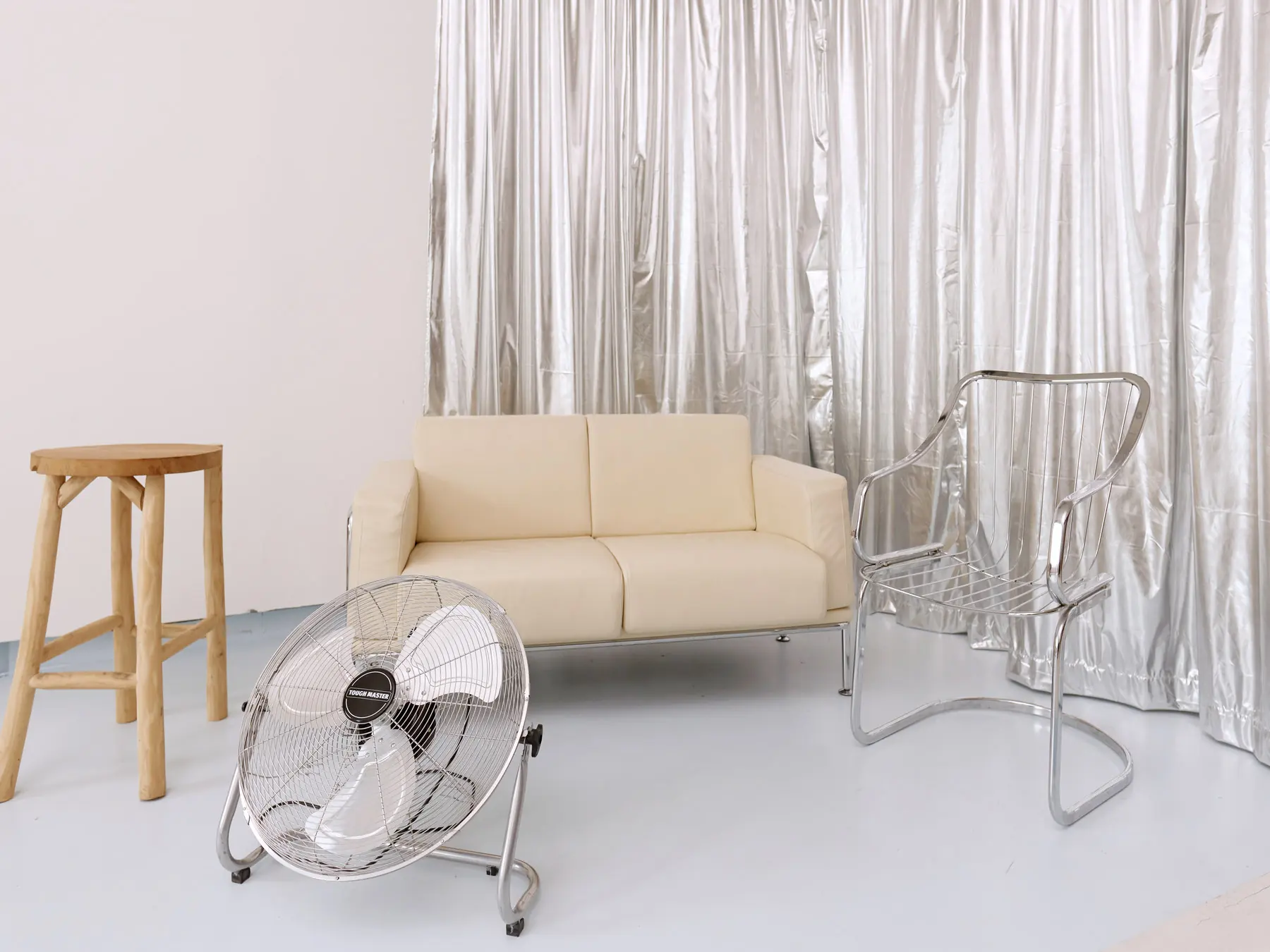 Fashion zāle: sudraba draperijas fons, krēmkrāsas ādas dīvāns, hroma krēsls un ventilators