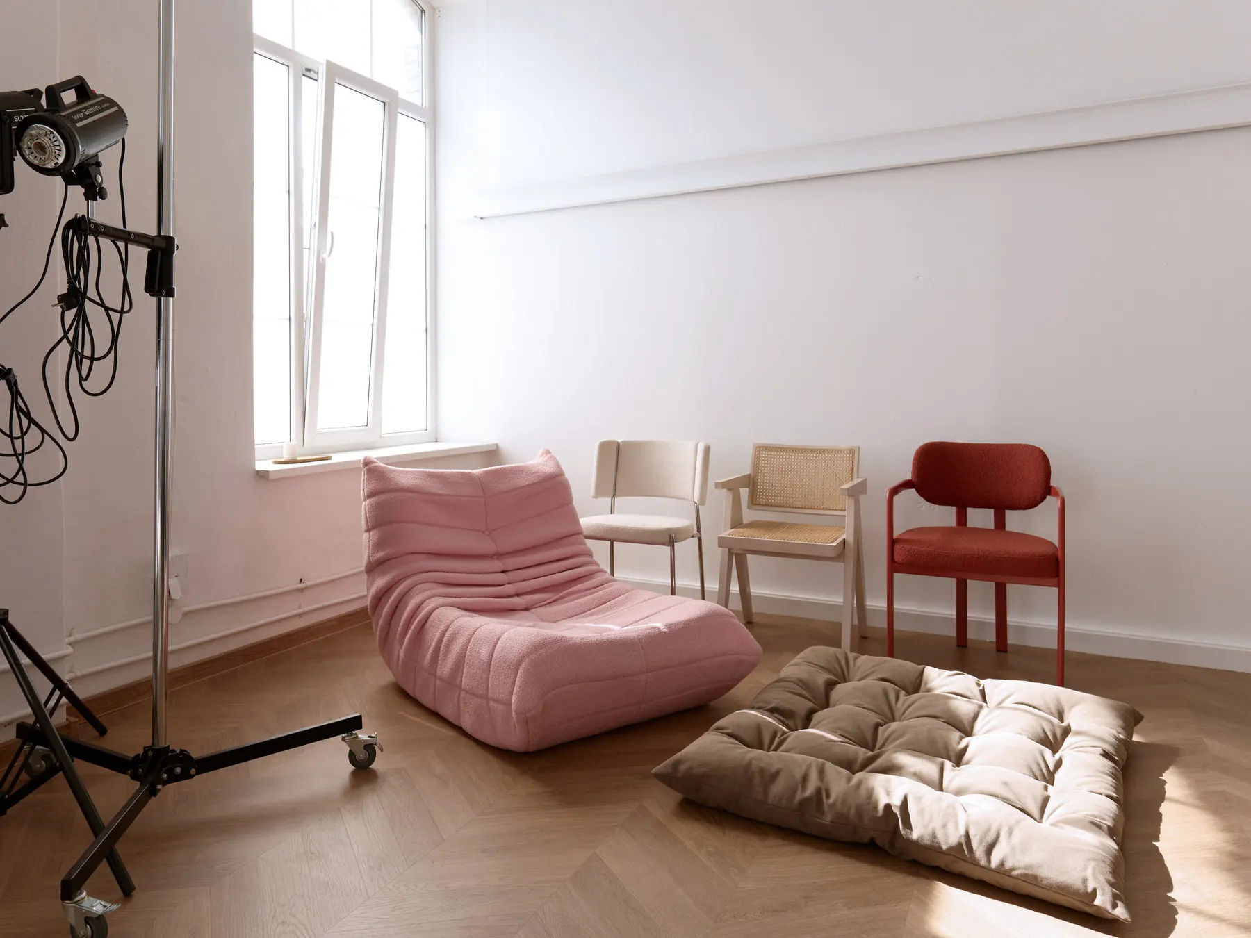 Home Chic zāle: rozā bukles atpūtas krēsls, trīs dizaina krēsli un liels grīdas spilvens pie loga